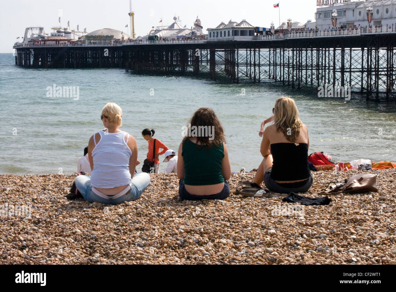 Three women sitting on Brighton beach. Brighton has two piers, Palace Pier which was opened in 1899 and West Pier which has been Stock Photo