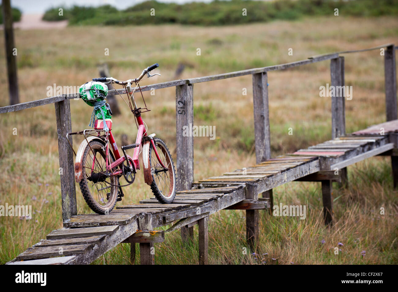 An old bicycle leaning against a rickety wooden handrail on a walkway on Mersea Island, the most easterly inhabited island in th Stock Photo