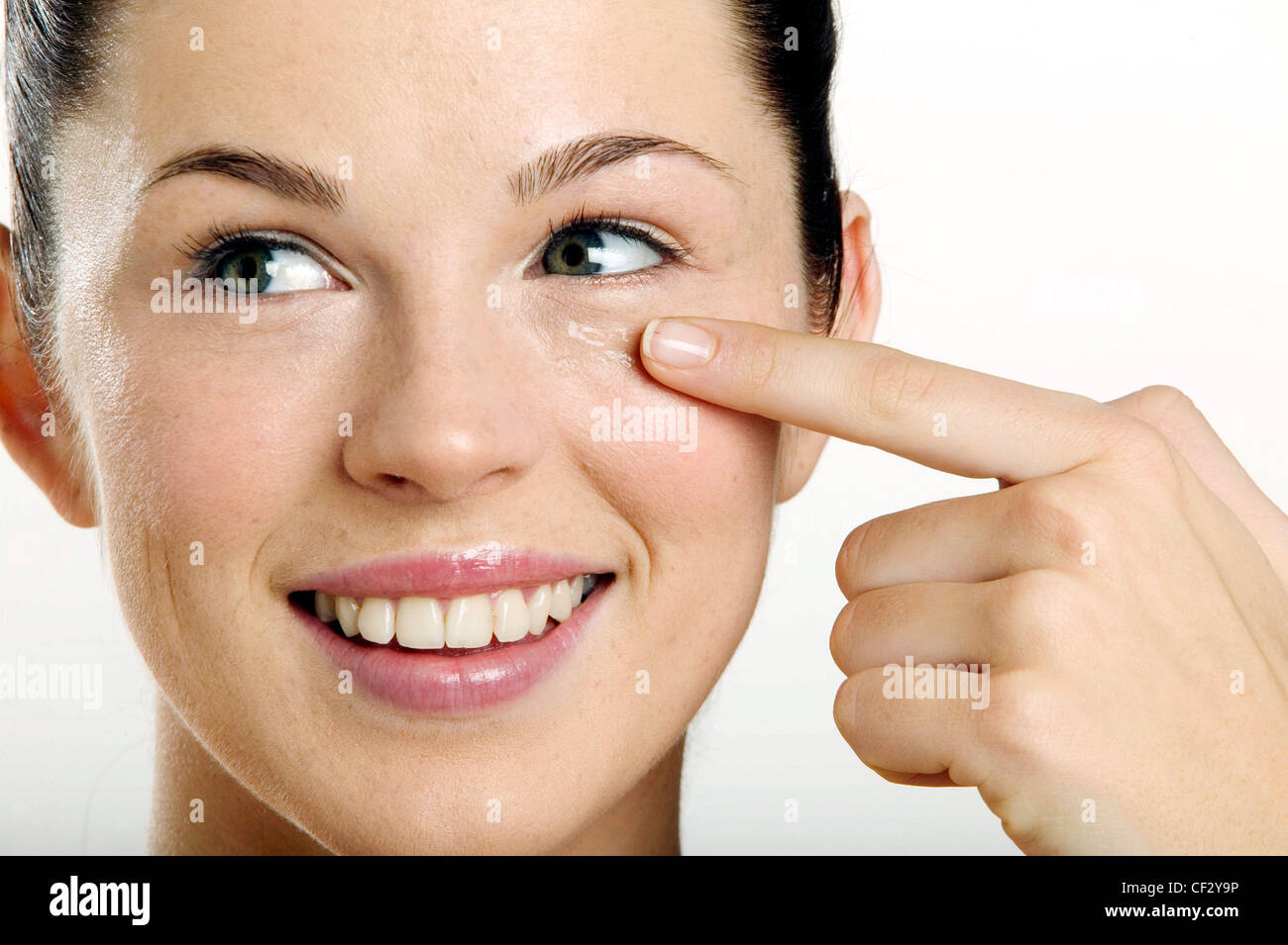 Female rubbing in clear eye gel under eye with finger, looking to side