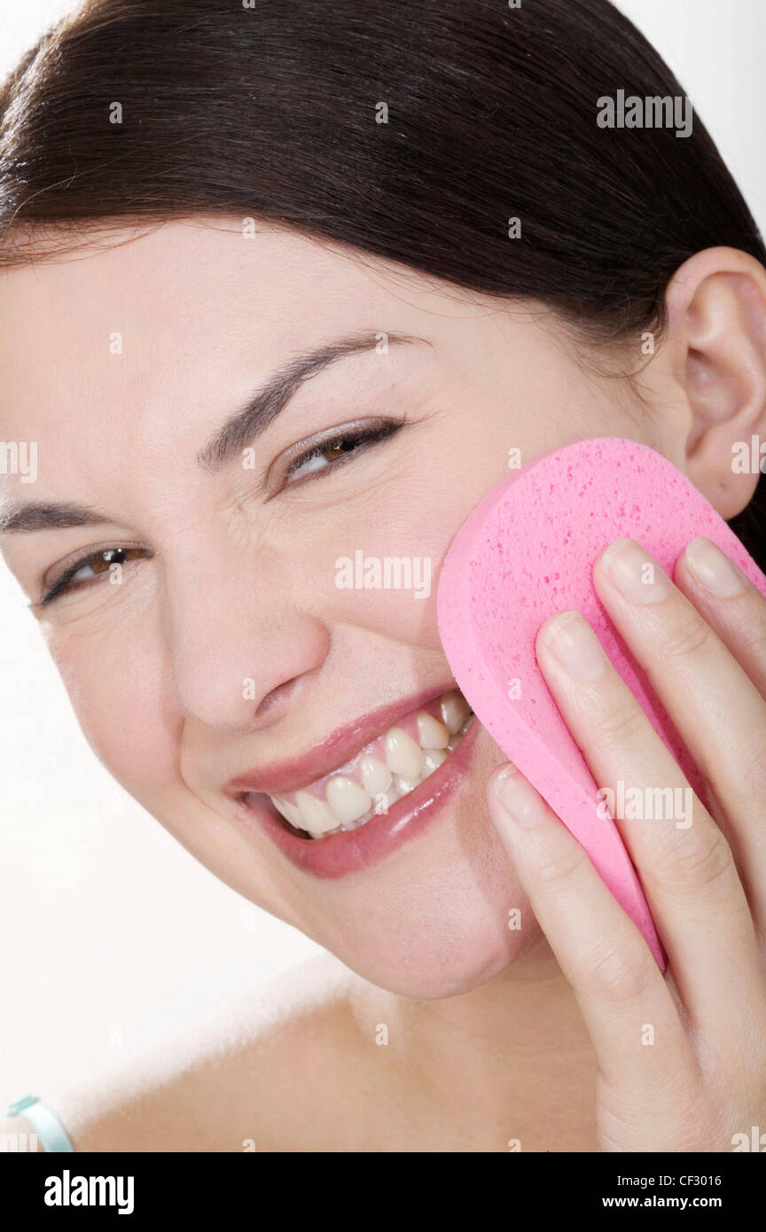 Female hair off face holding pink facial sponge to cheek head