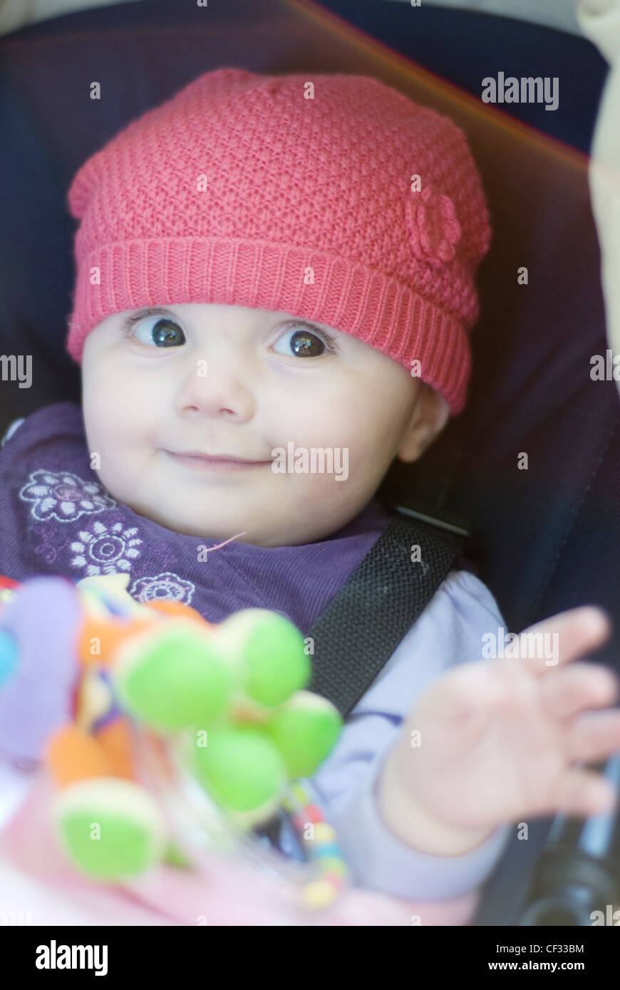 A female baby, wearing a purple dress and red hat, sitting in pushchair