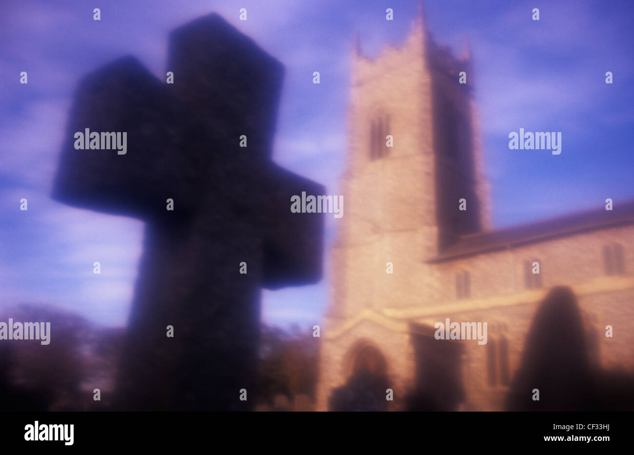 Atmospheric view in warm light of 15th century Perpendicular Gothic church and tower with silhouetted crucifix Stock Photo