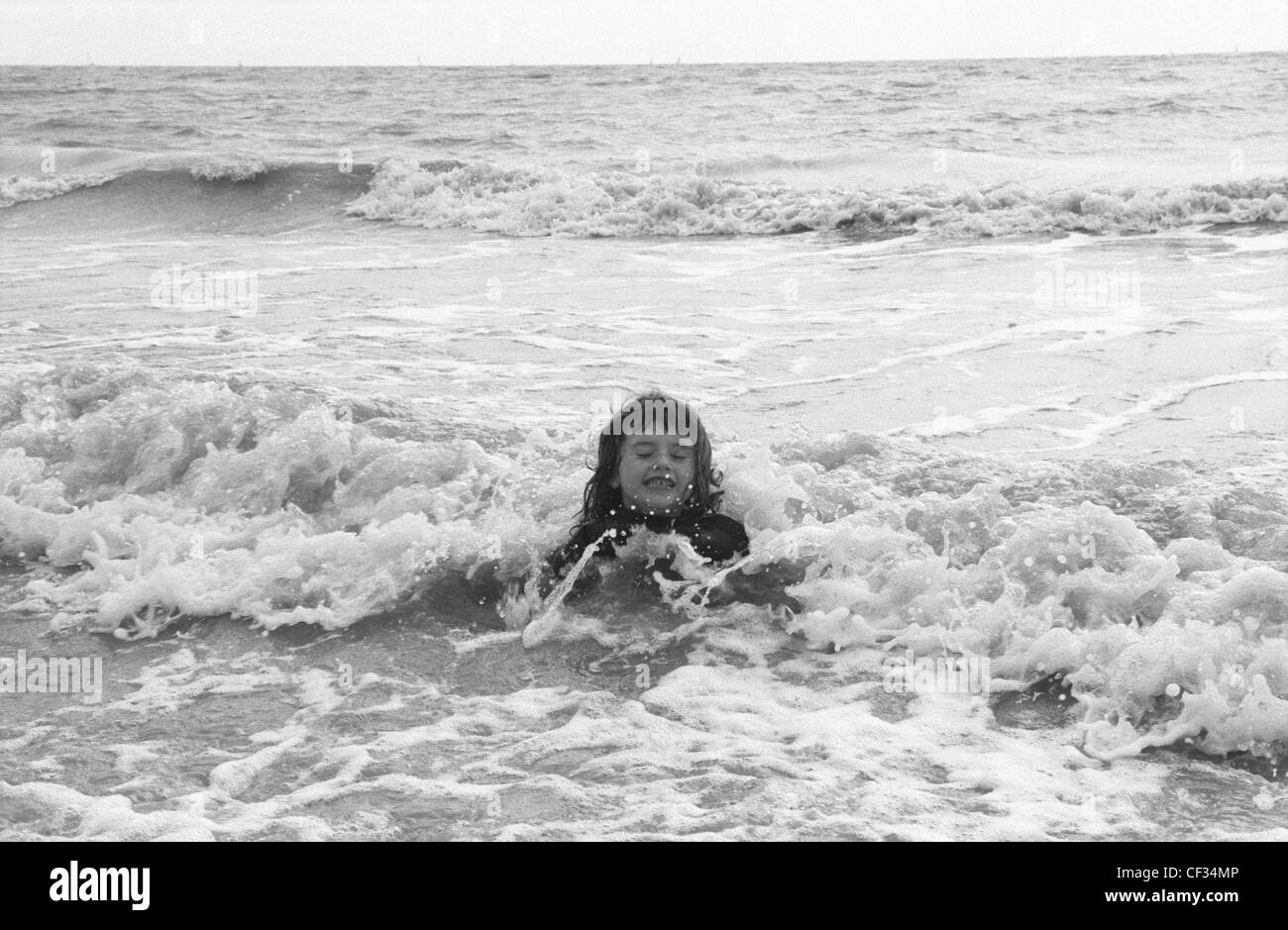 Female child lying down in waves in sea Stock Photo - Alamy