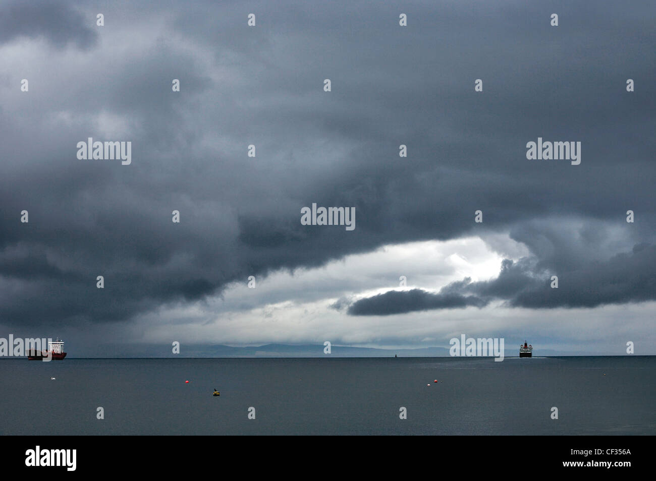 Stormy skies over a cargo ship and The MV Caledonian Isles, a ferry that operates between Ardrossan on the Ayrshire coast and Br Stock Photo
