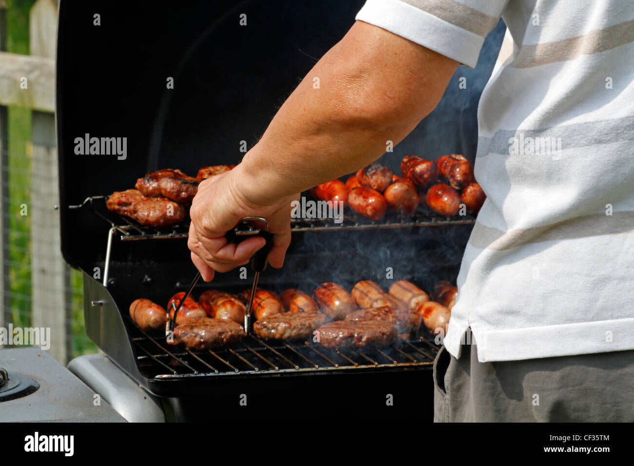 A man cooking sausages and burgers on a barbecue. Stock Photo