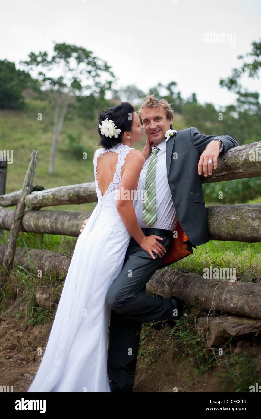 Bride embracing the Groom against a fence and groom looking to camera Stock Photo