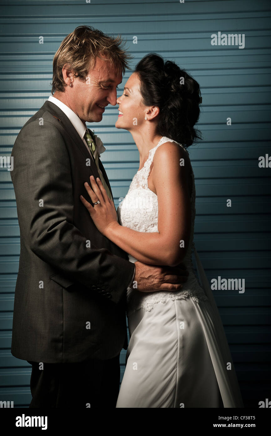 Bride and Groom touching noses against a blue wall and laughing Stock Photo