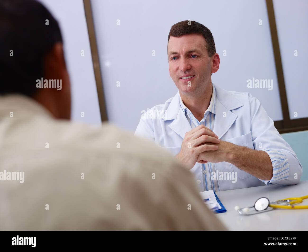 Friendly doctor working and giving assistance to old male patient in hospital office. Focus on background Stock Photo