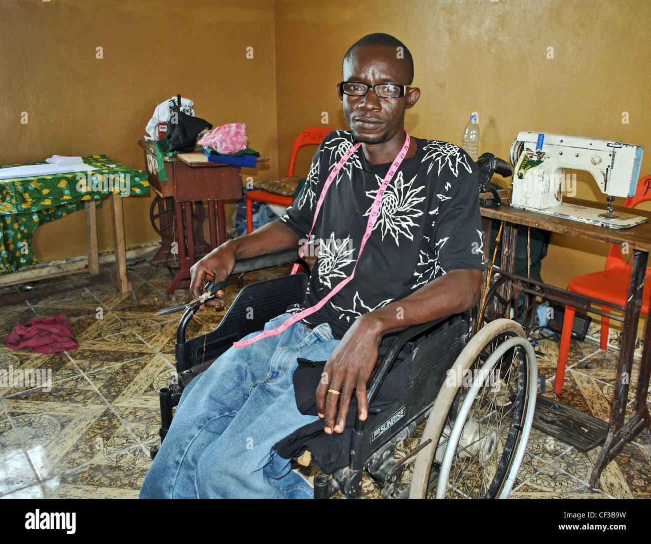 A man with polio works as a tailor in a UNDP-funded employment project in Makeni, Sierra Leone Stock Photo
