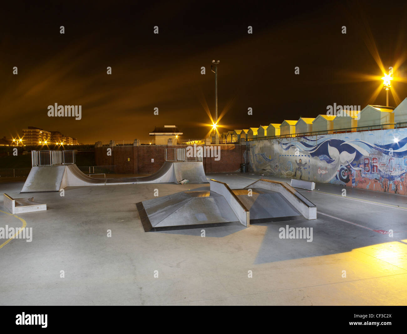 An empty concrete skatepark at night with a line of beach huts overlooking it in East Sussex. Stock Photo