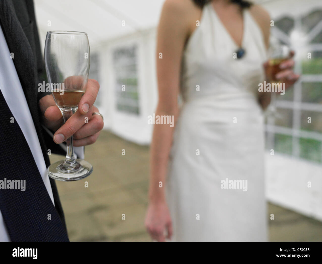 Close up of a man holding a nearly empty glass with a woman in white holding a full glass of champagne. Stock Photo