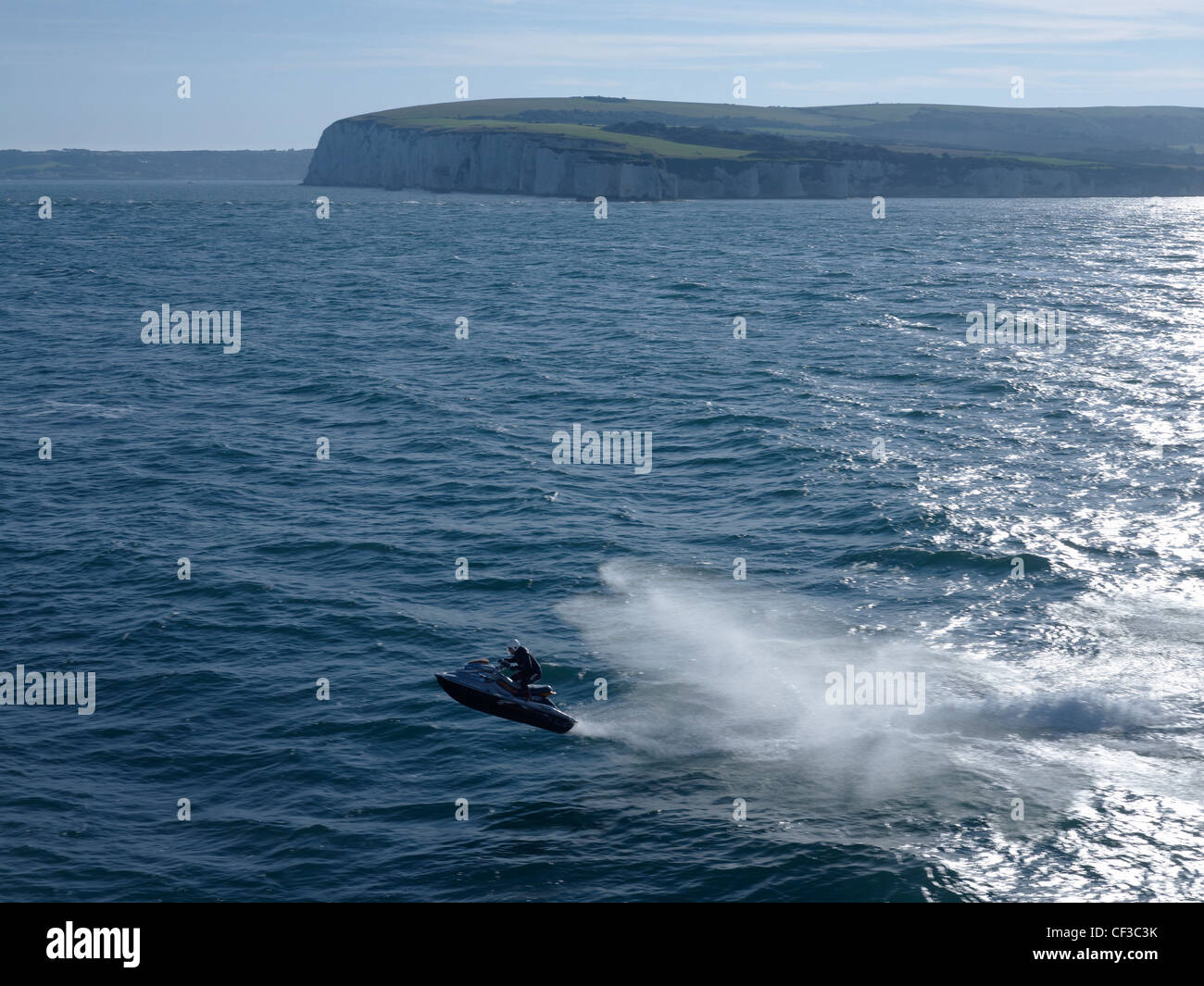 A jetskier jumping out of the sea with white cliffs and headland in the background. Stock Photo