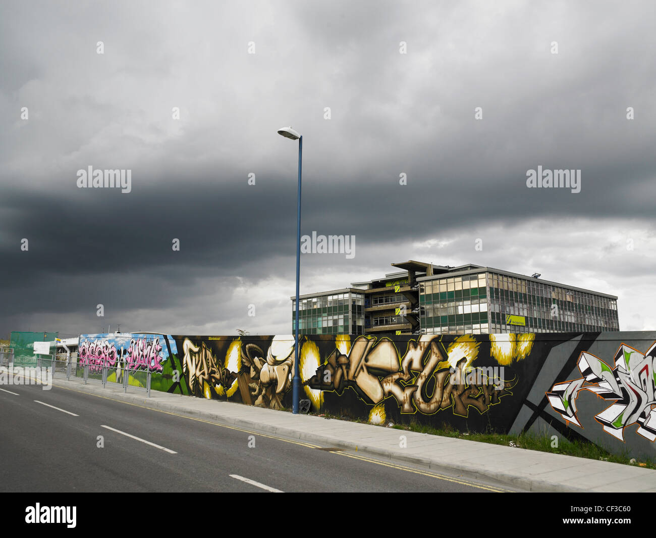 Graffiti on hoardings in front of a sixties style building with heavy grey cloud above in Brighton. Stock Photo