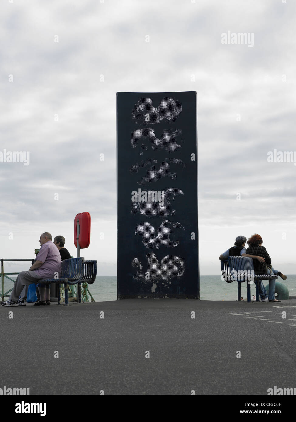 A sculpture of people kissing with two couples sitting either side on the water front in Brighton. Stock Photo