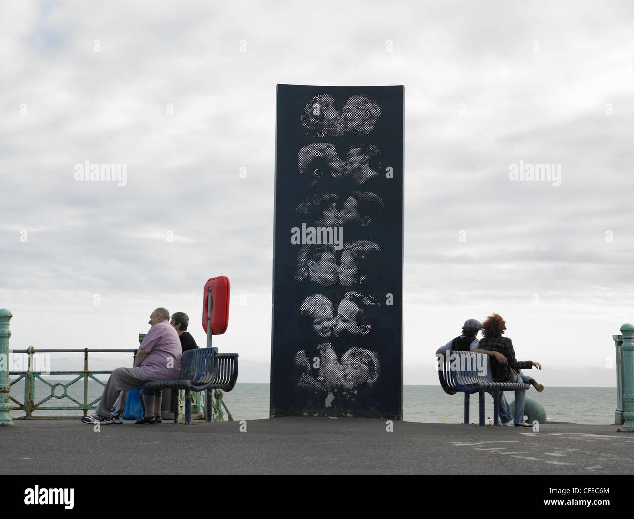 A sculpture of people kissing with two couples sitting either side on the water front in Brighton. Stock Photo