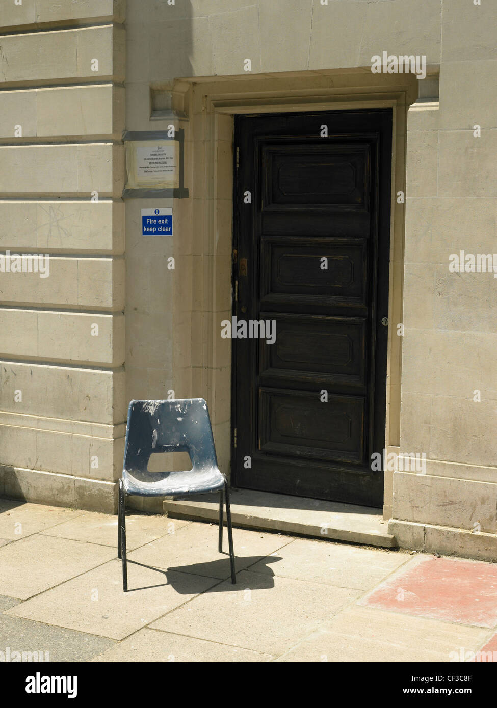 A blue plastic chair in front of a wooden door on a bright sunny day in Brighton. Stock Photo