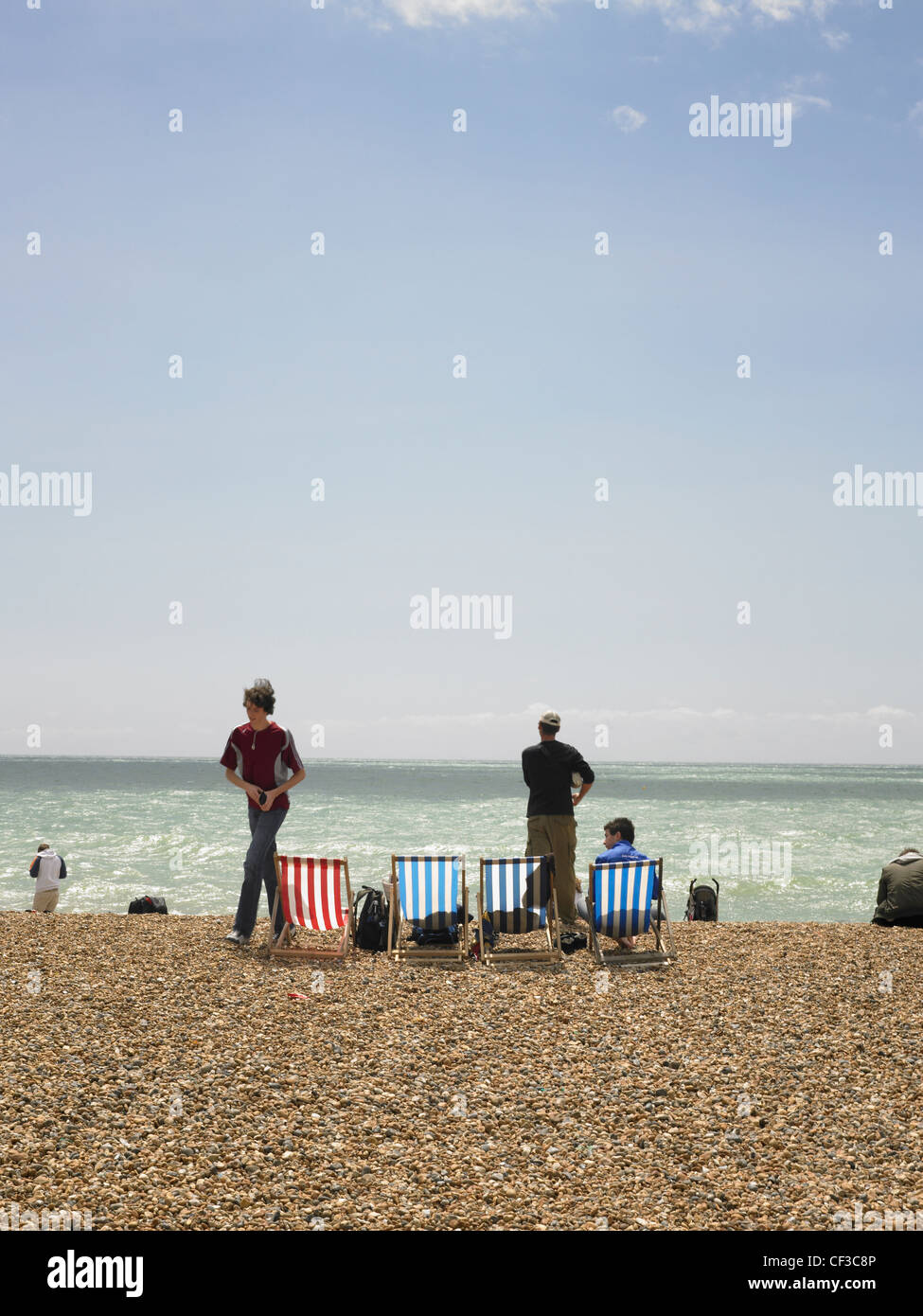 Deckchairs and people on Brighton beach on a sunny day with blue sky. Stock Photo