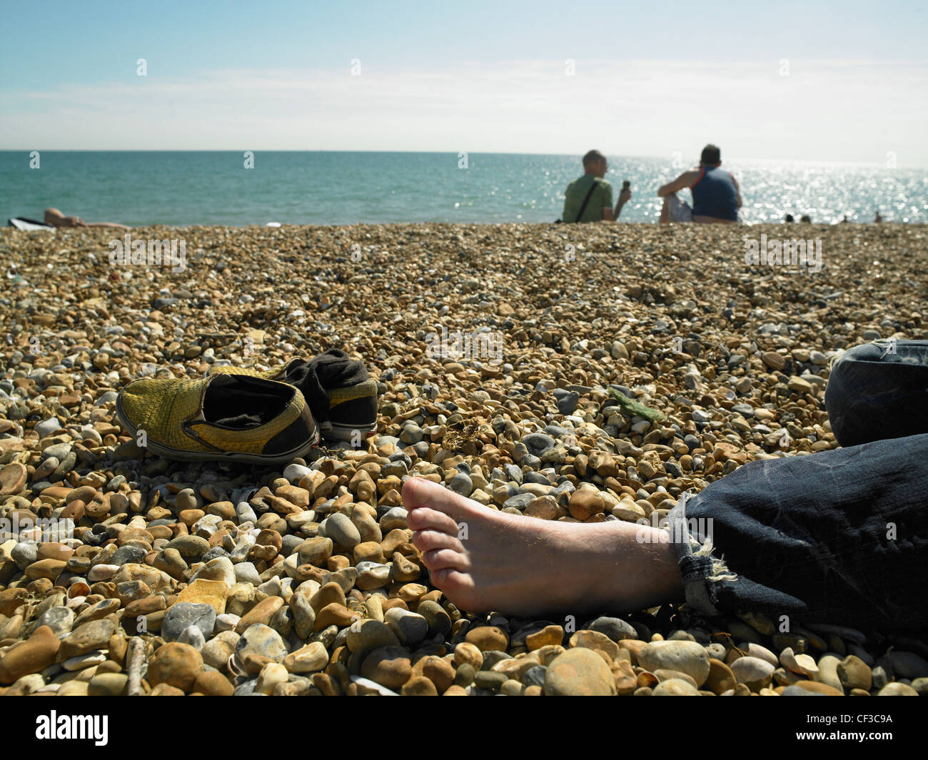 Detail of a bare foot and shoes laying on the beach in Brighton. Stock Photo