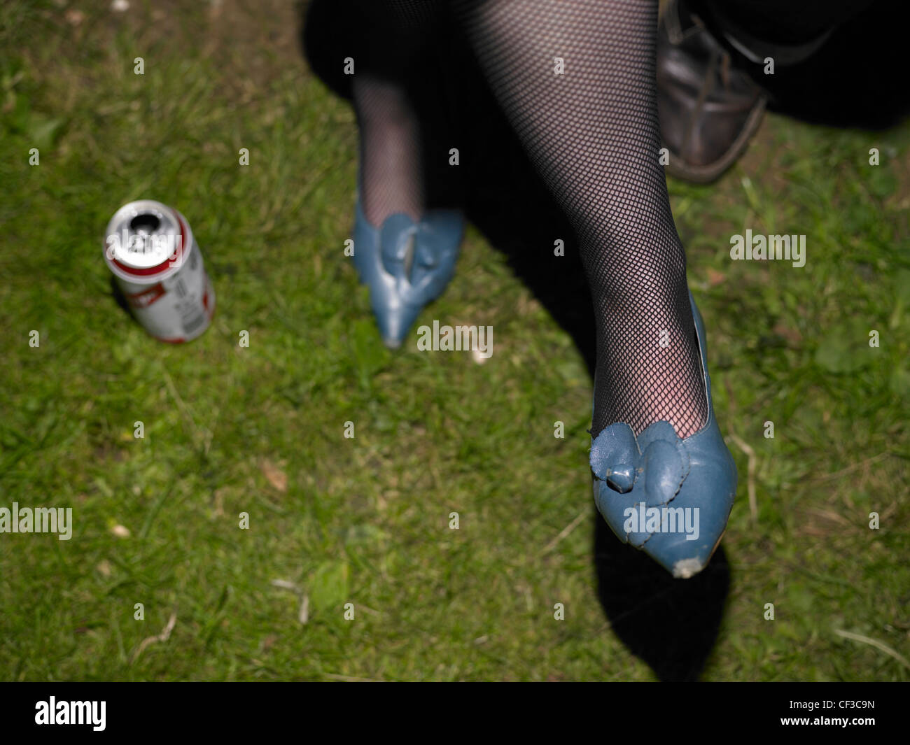 A can of beer on the ground next to a womans legs in fishnet stockings at a festival in Brighton. Stock Photo