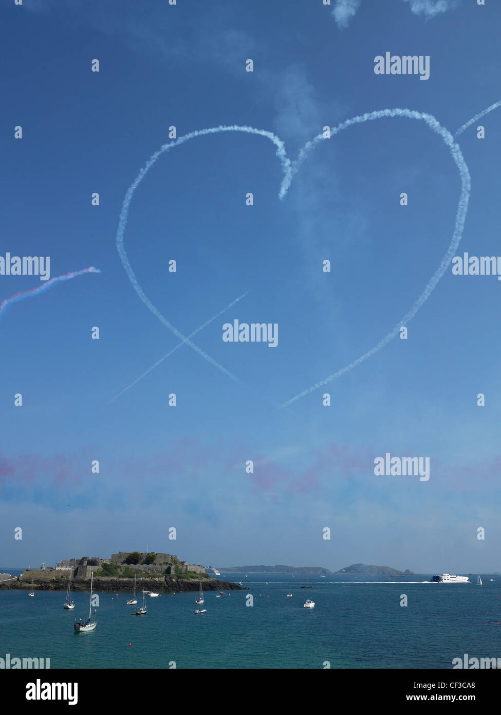 A heart made of smoke hangs in a blue sky over Castle Cornet in Guernsey after a Red Arrows display. Stock Photo