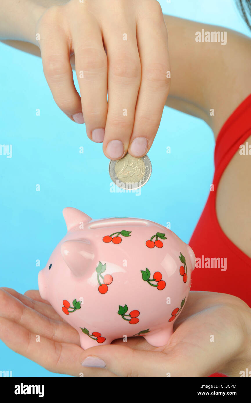 Female wearing red vest, putting a coin into piggy bank Stock Photo - Alamy