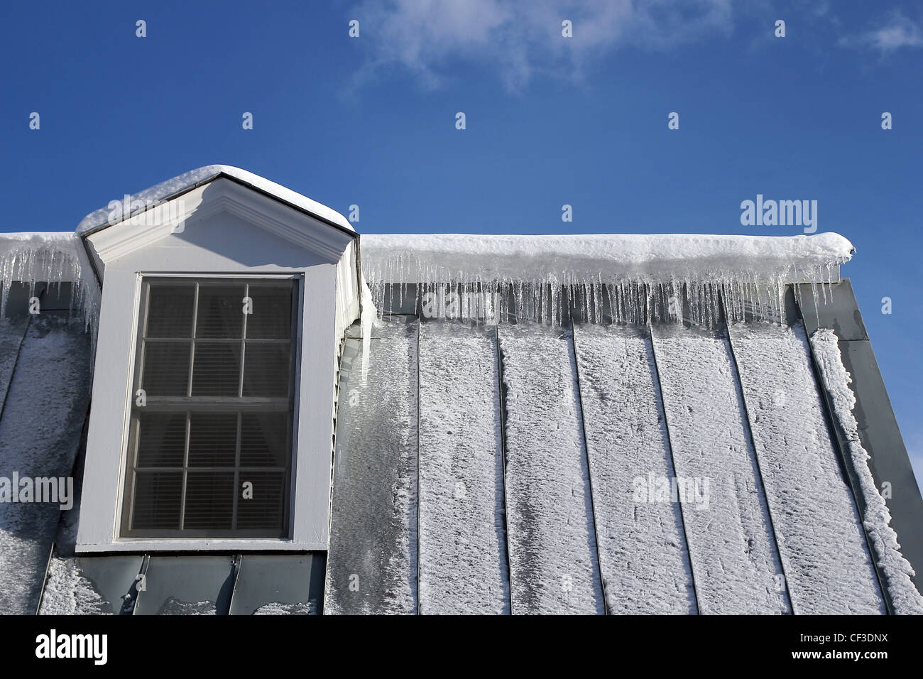 Icicles hanging over a metal roof on a building in Vermont under a blue sky Stock Photo