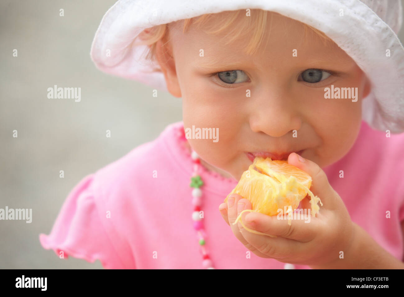 little girl wearing panama hat is eating orange. focus on orange in