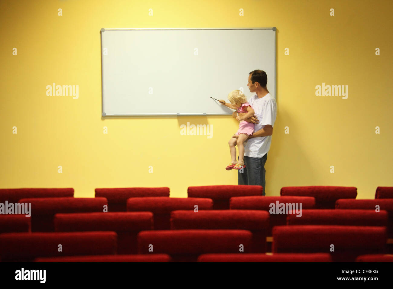 father and little girl in empty presentation hall. little girl is drawing on a board Stock Photo