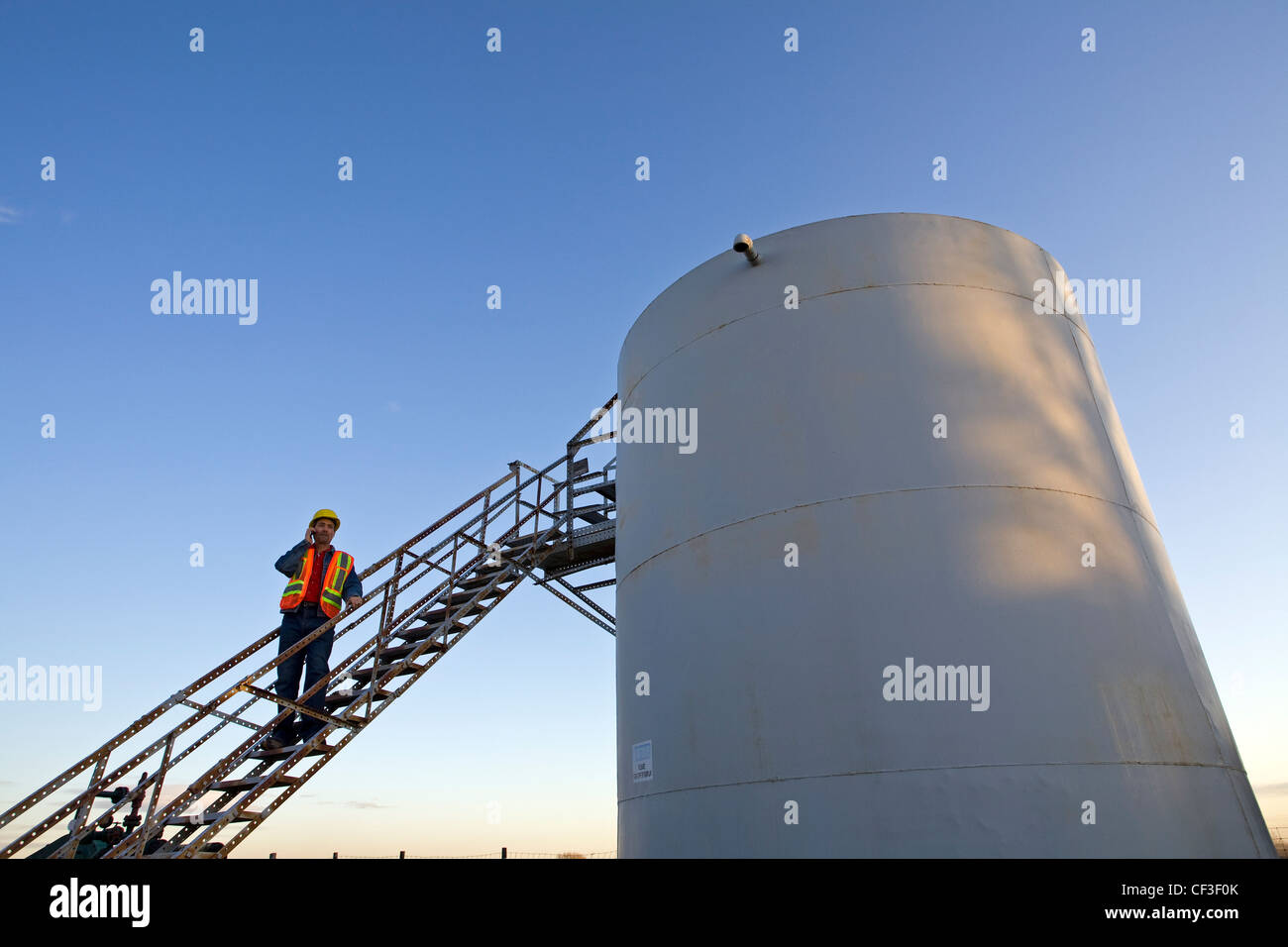 Oil industry worker on storage tank platform talking on phone. Stock Photo