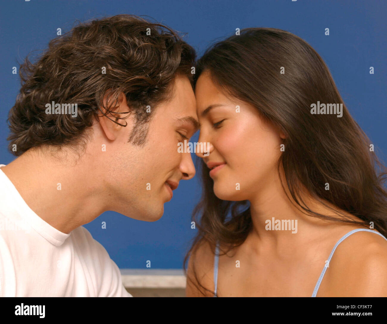 Semi profile of female long brunette hair wearing pale blue vest top looking at boyfriend leaing forehead against his smiling Stock Photo