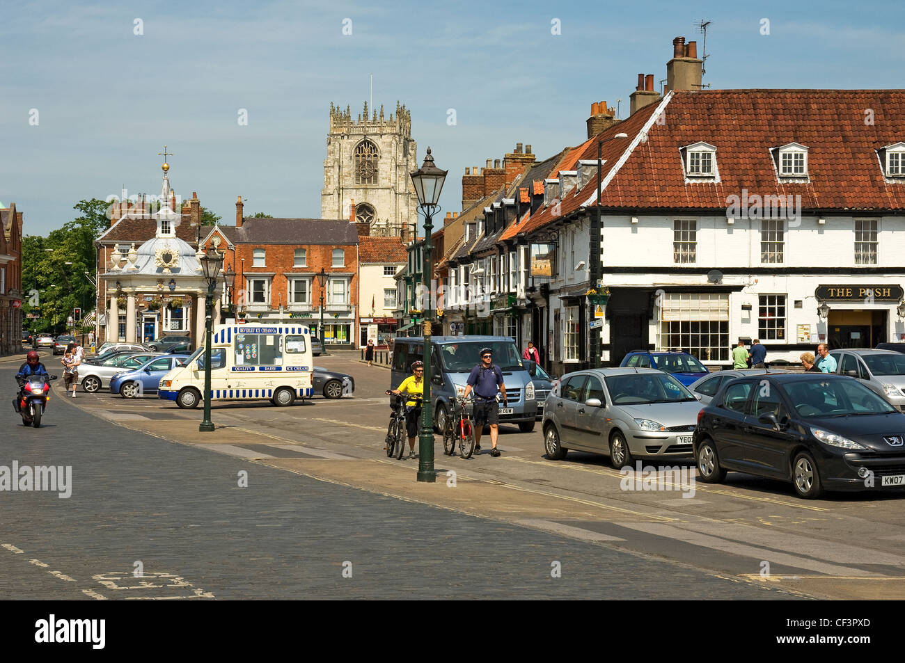 Two cyclists walk their bicycles past Market Cross in Saturday Market, Beverley. Stock Photo