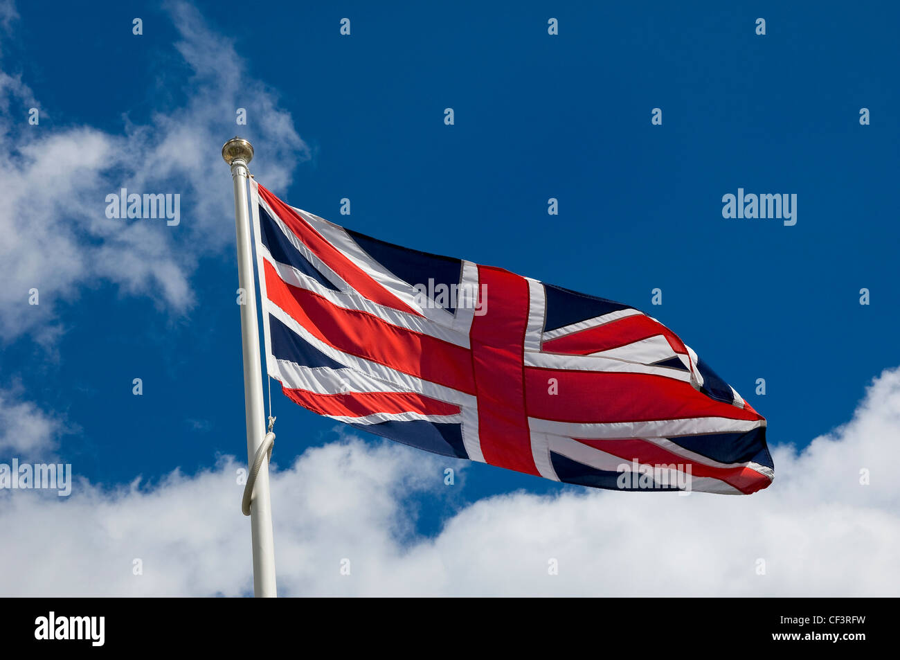 A union flag on a flagpole fluttering in the breeze against a blue sky. Stock Photo