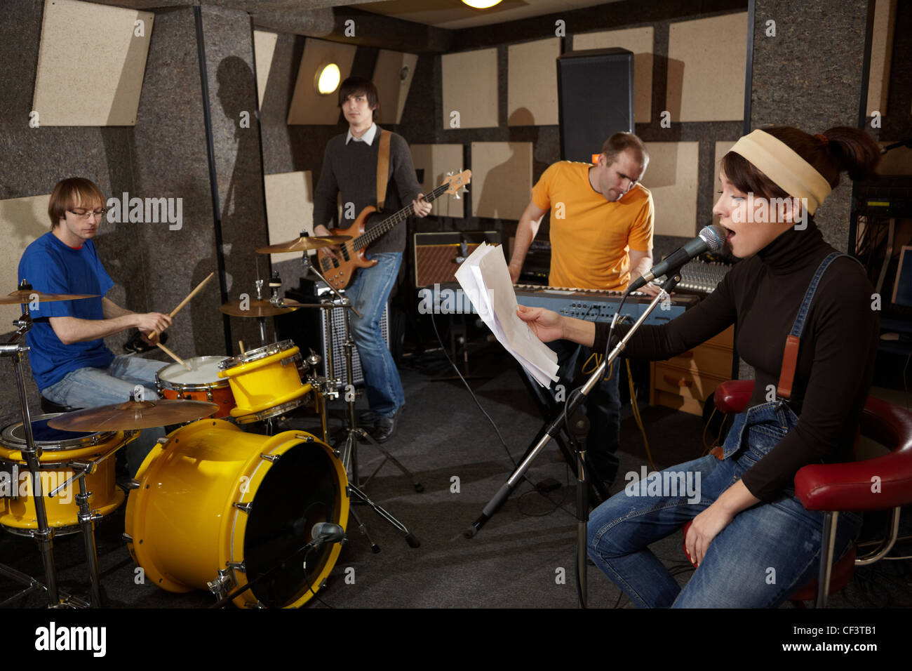 a rock band is working in studio. vocalist girl is singing with text of song in the her hand Stock Photo