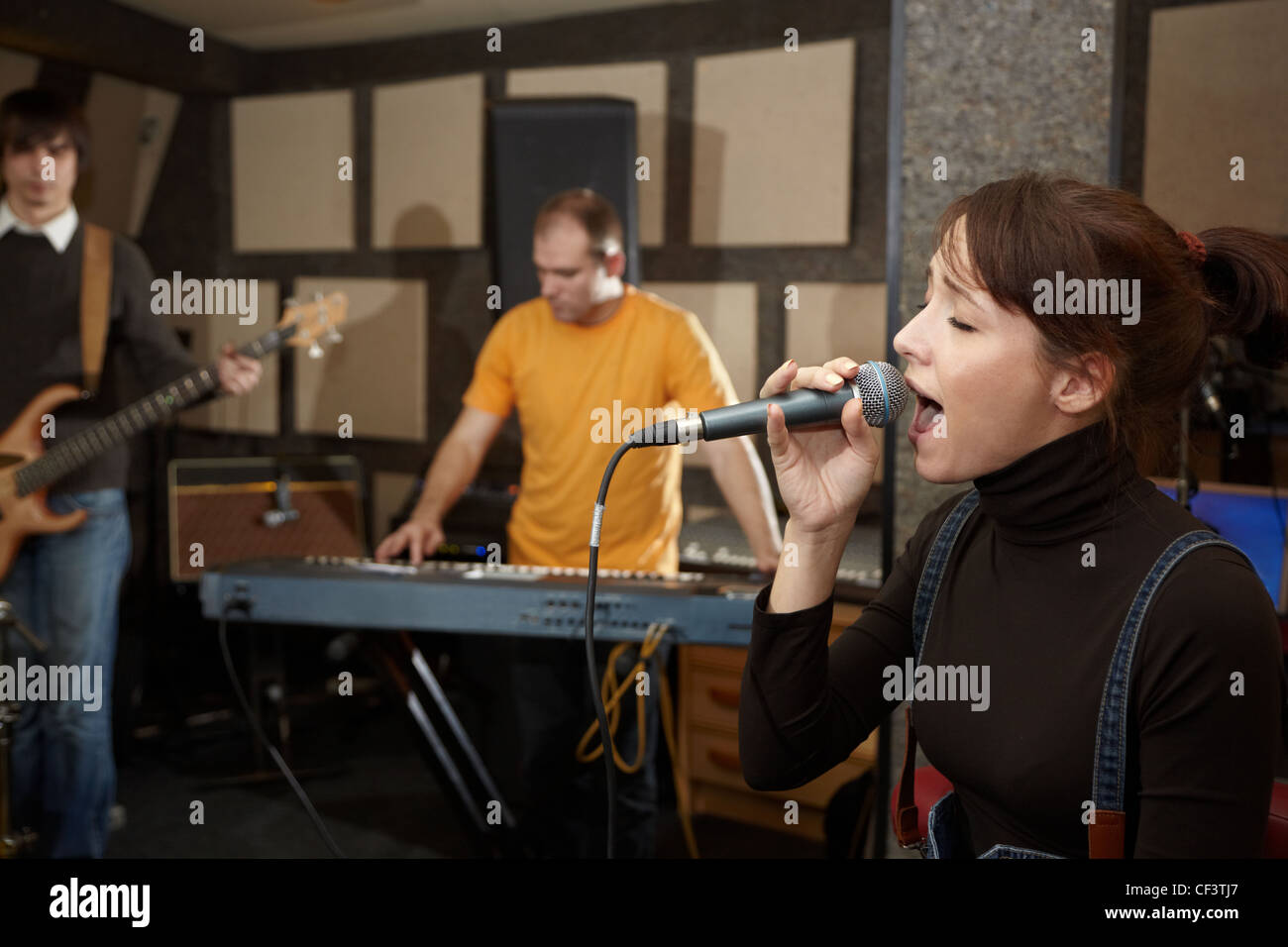 vocalist girl is singing. electro guitar player and keyboarder in out of focus Stock Photo
