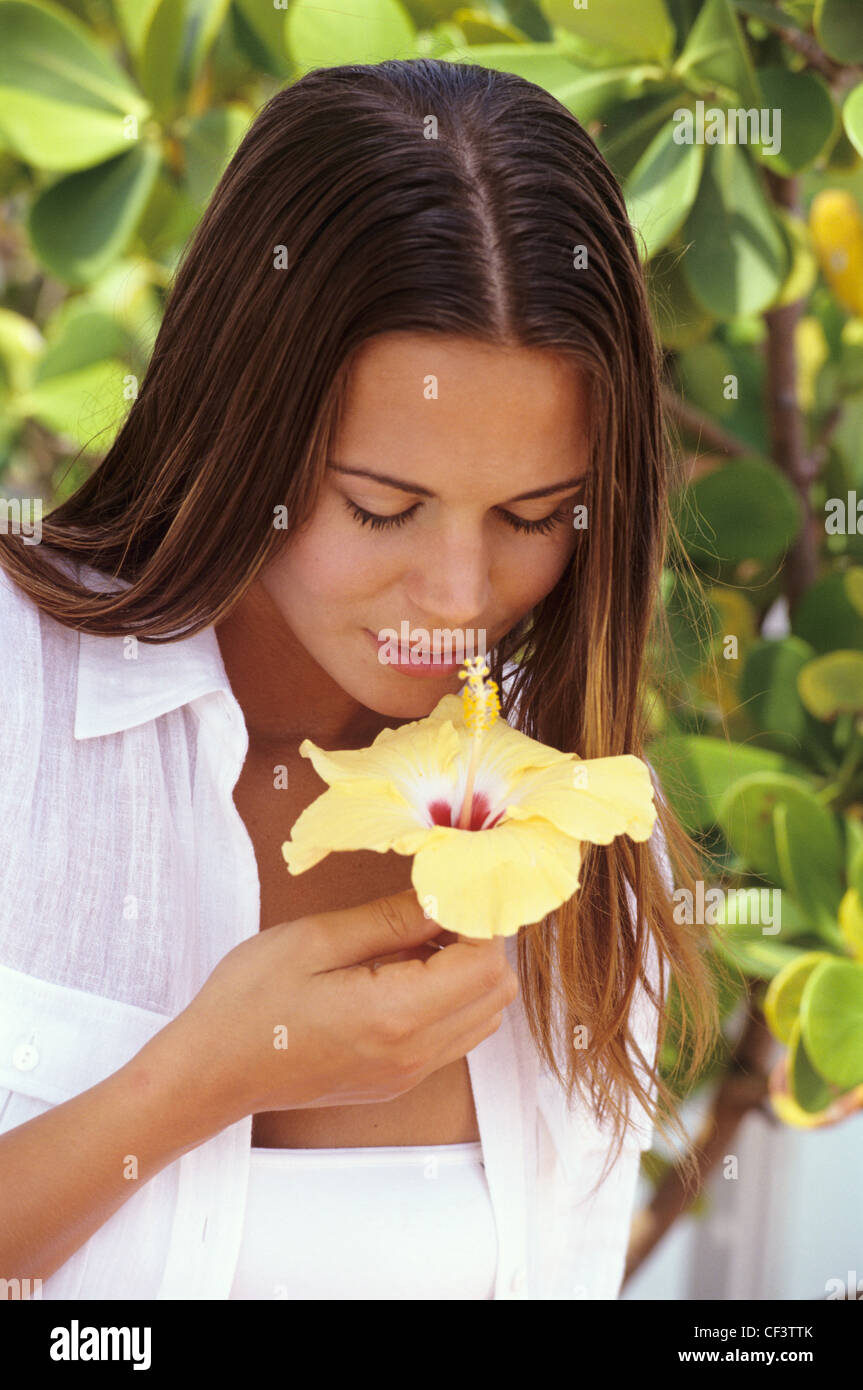 Female long brunette hair leaning forward smelling large yellow hibiscus flower, looking down smiling, plants in background Stock Photo - Alamy Female long brunette hair leaning forward smelling large yellow hibiscus flower, looking down smiling, plants in background Stock Photo - Alamy