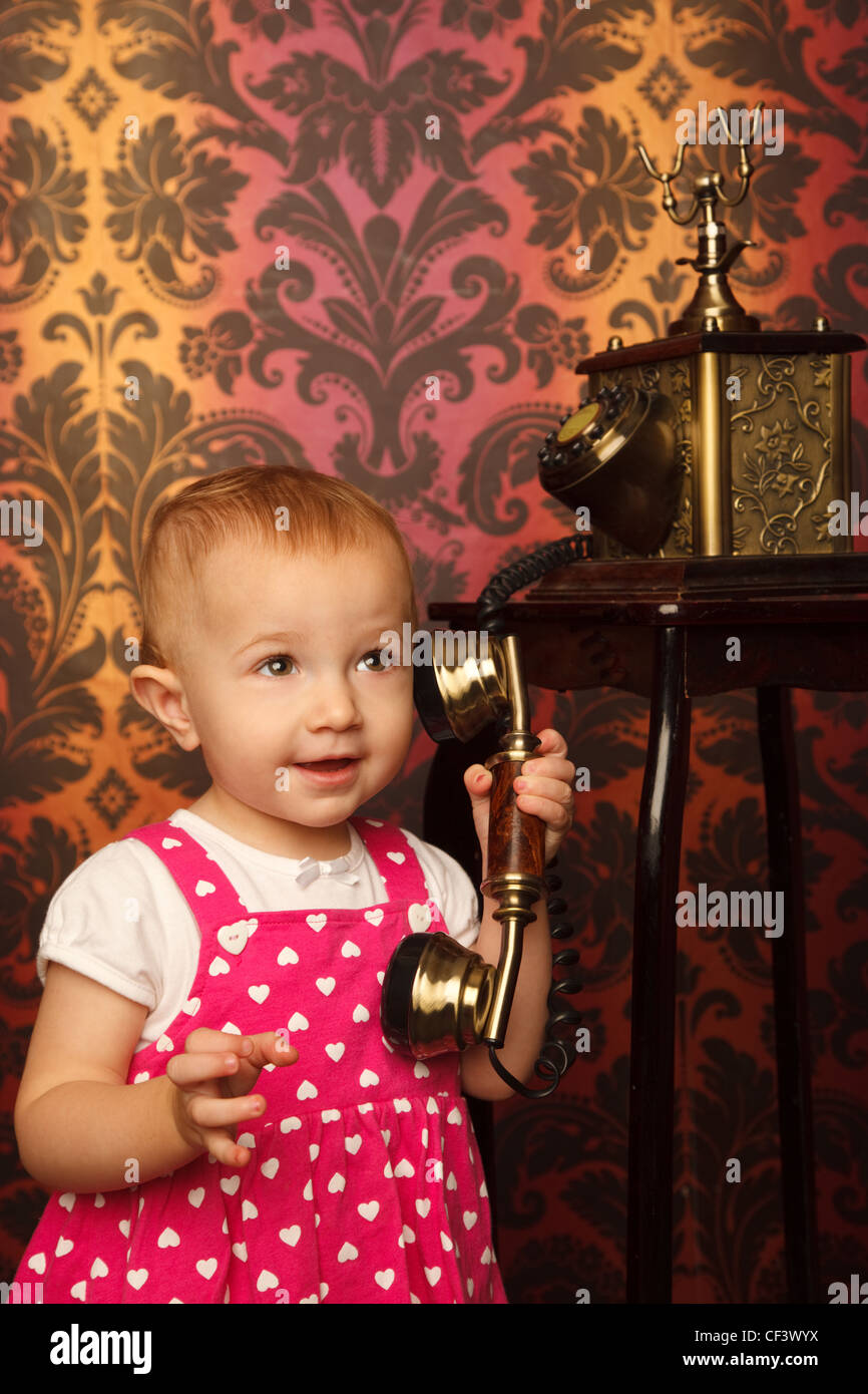 Little girl in red dress talking vintage phone. Interior in retro style. Vertical format. Stock Photo
