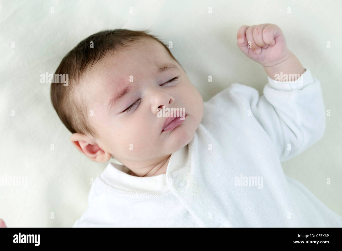 Male Child With Dark Brown Hair Wearing White Babygrow Lying On