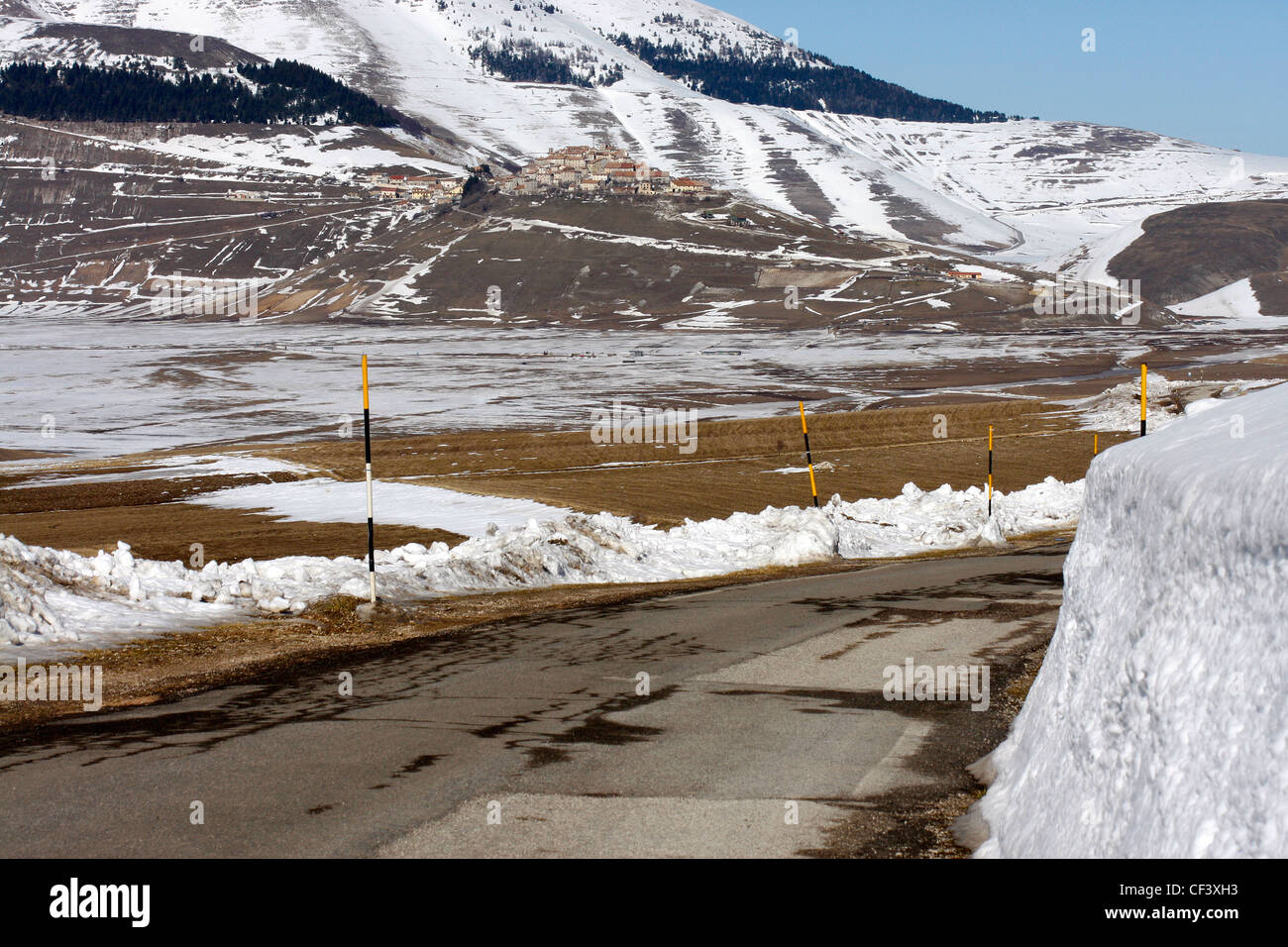 Winter snow view of Castelluccio  across the Piano Grande with depth of snow  pole indicators along the road. Stock Photo