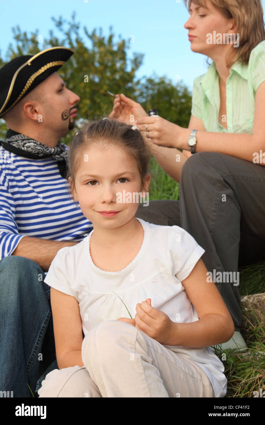 family in early fall park. little girl in focus. woman drawing funny whiskers and beard on man's face in out of focus. Stock Photo