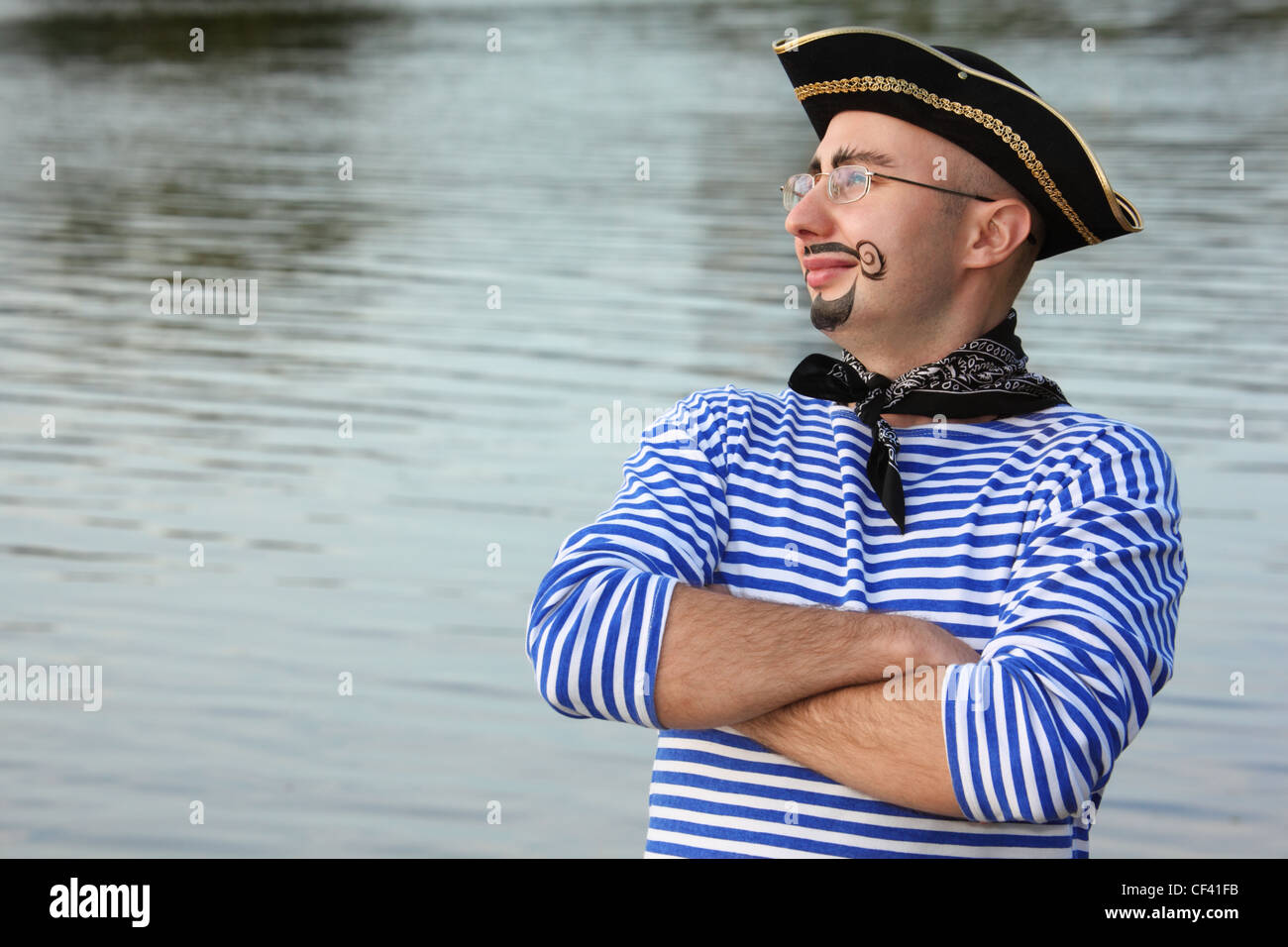 man with drawed beard and whiskers in pirate suit near pond is looking away Stock Photo