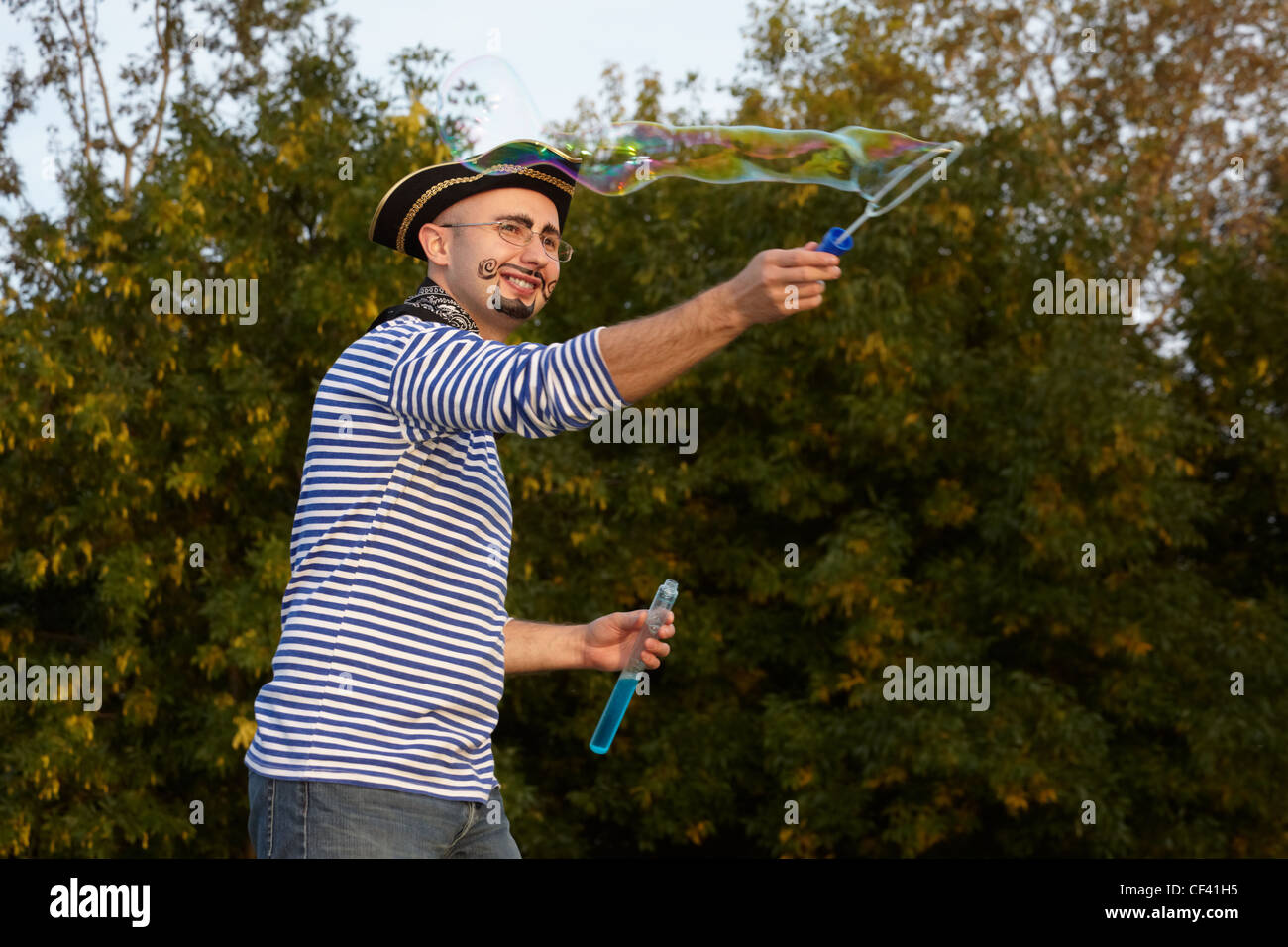 joyful man with drawed beard and whiskers in pirate suit is blowing soap bubbles. Stock Photo