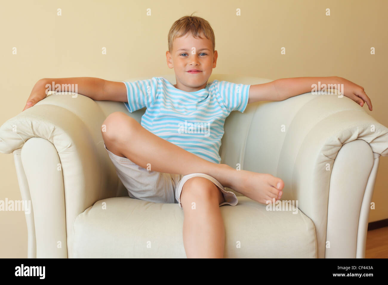 boy freely sitting with magnificent easy chair in cosy room Stock Photo