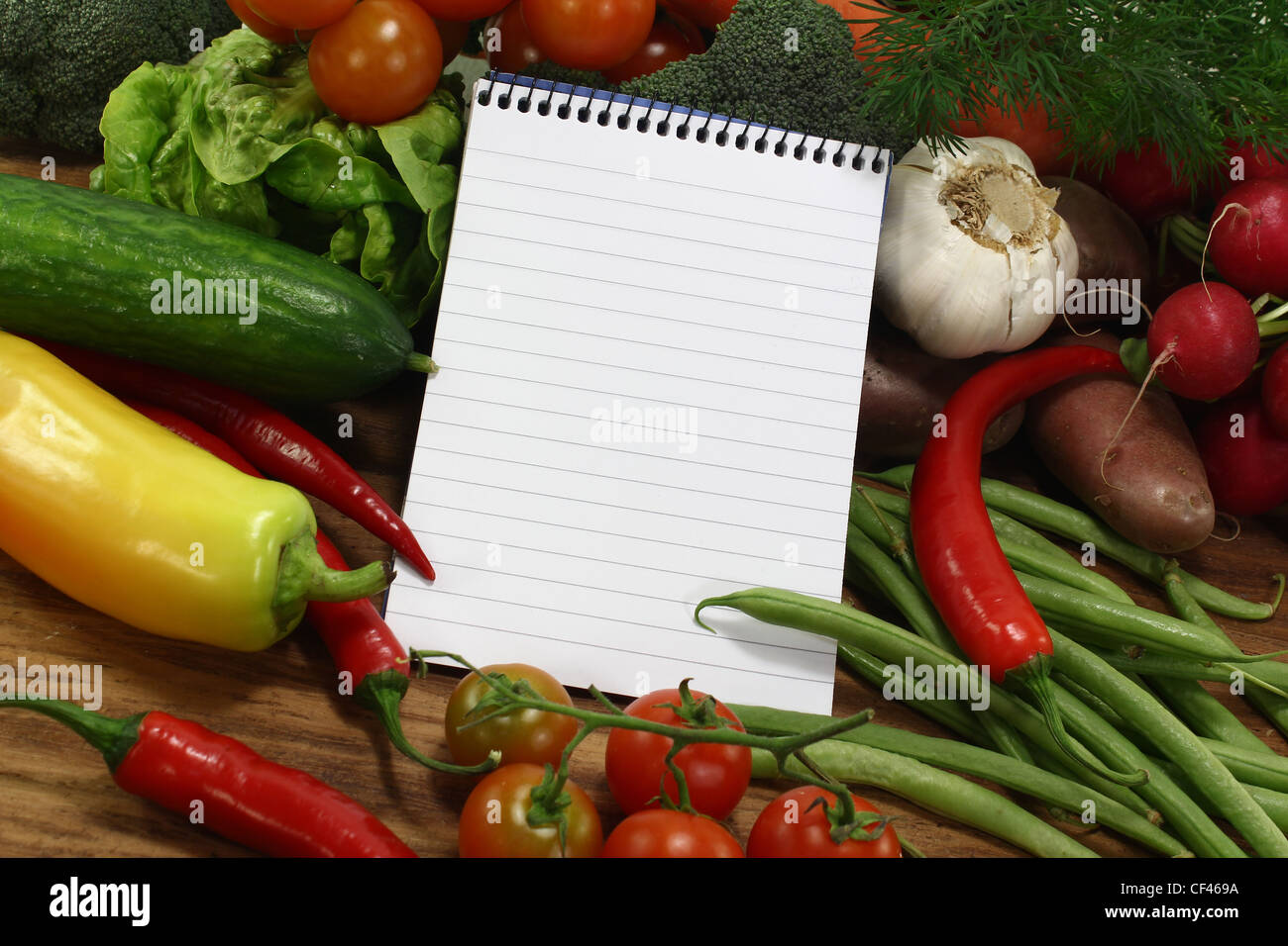 little ruled shopping list with vegetables on a wooden background Stock