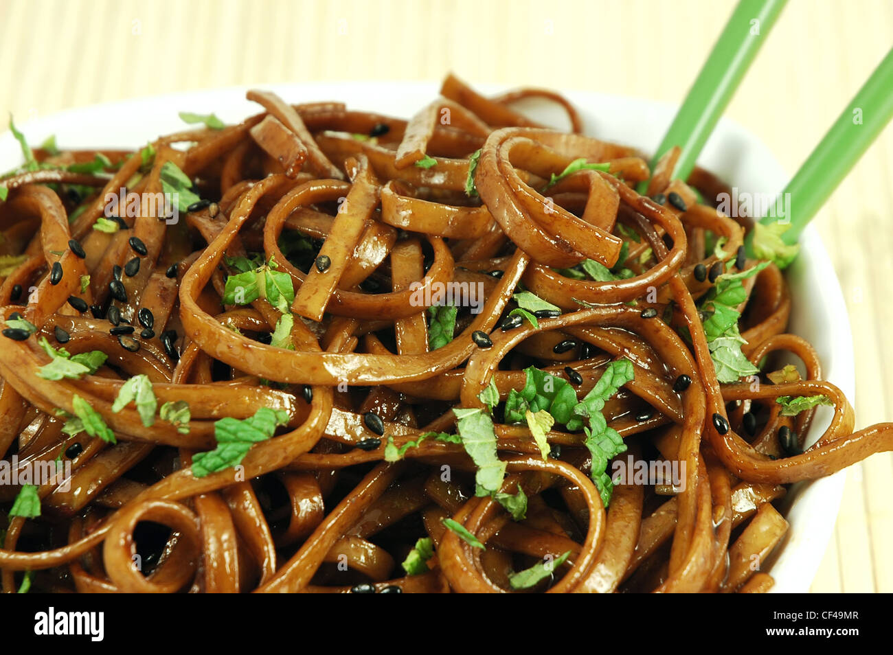 Bowl of stir fried udon noodles garnished with black sesame seeds and fresh mint with green chopsticks Stock Photo