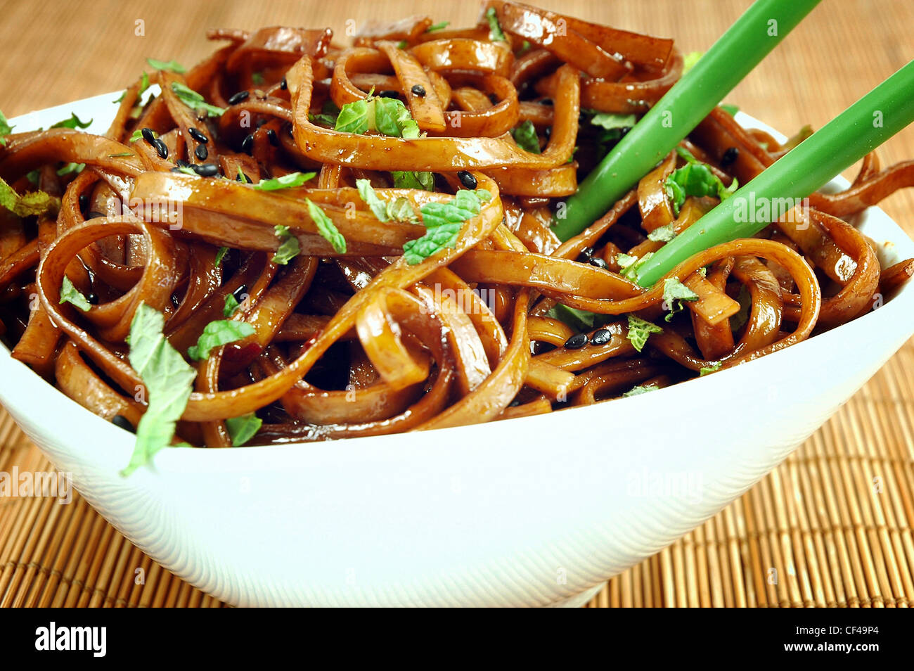 Bowl of stir fried udon noodles garnished with black sesame seeds and fresh mint with green chopsticks Stock Photo