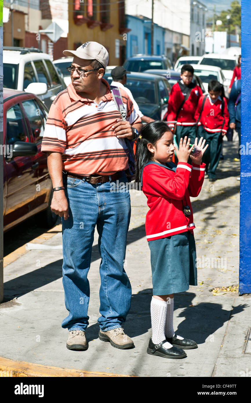 casually dressed dutiful Mexican dad patiently walking his playful young daughter in school uniform home from classes Oaxaca Stock Photo