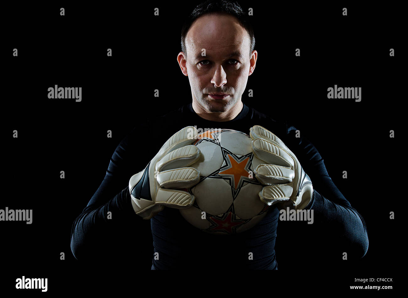 Portrait of football goalkeeper on black background. Man is wearing goalie gloves and goalkeeper's blouse. Studio shot Stock Photo