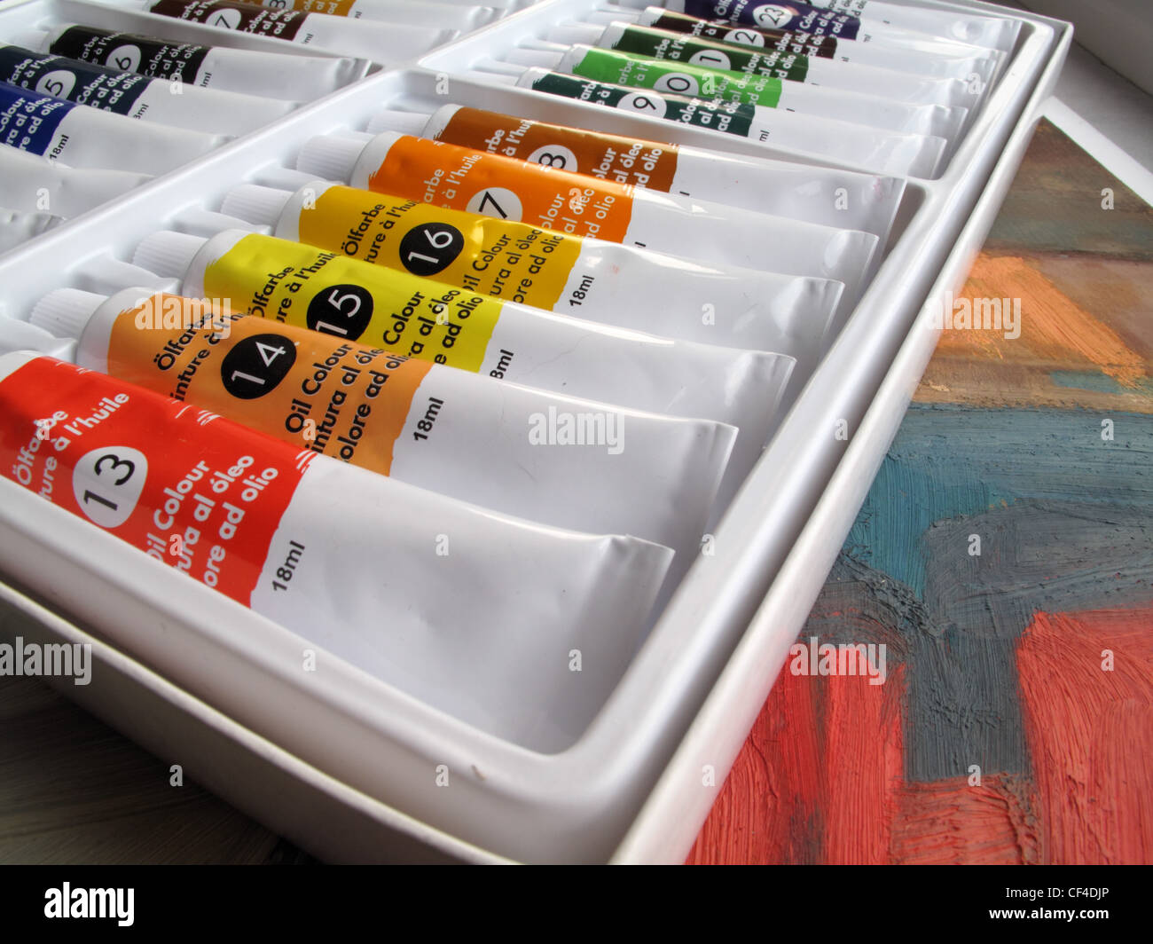 A box of new oil paints sits on top of a painted canvas. Stock Photo