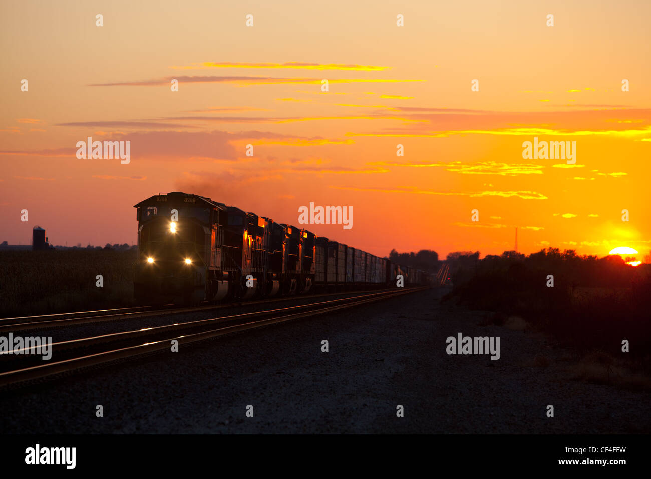 Freight train rolls out of a colorful sunset. Stock Photo