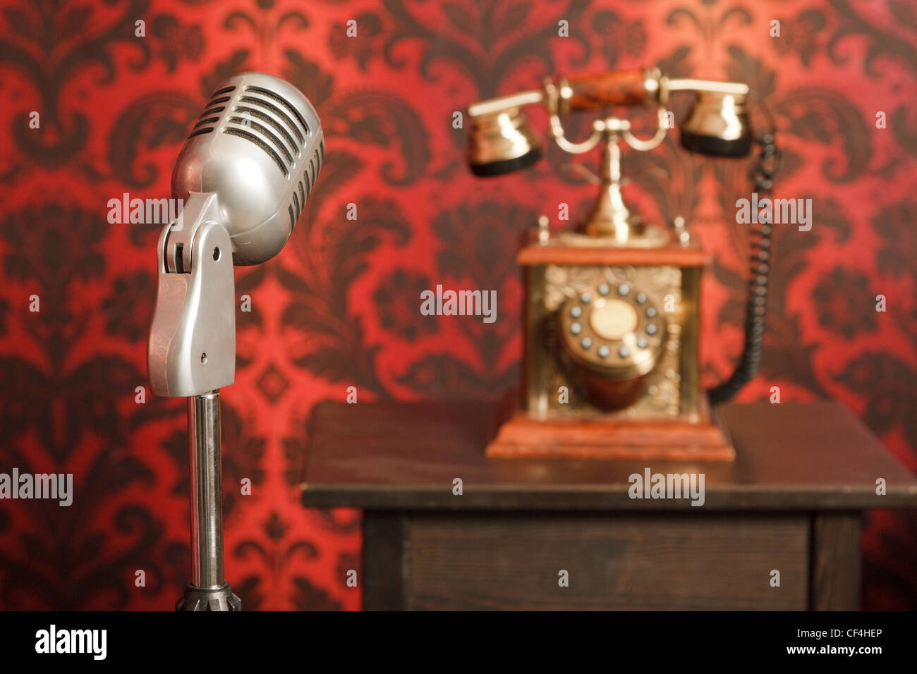 vintage microphone on a stand, in the background an old phone made from metal stands on a wooden table. Focus on the microphone Stock Photo